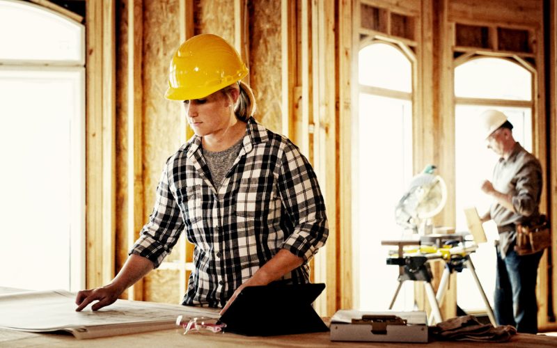 Woman architect looking over blueprints at home construction site.